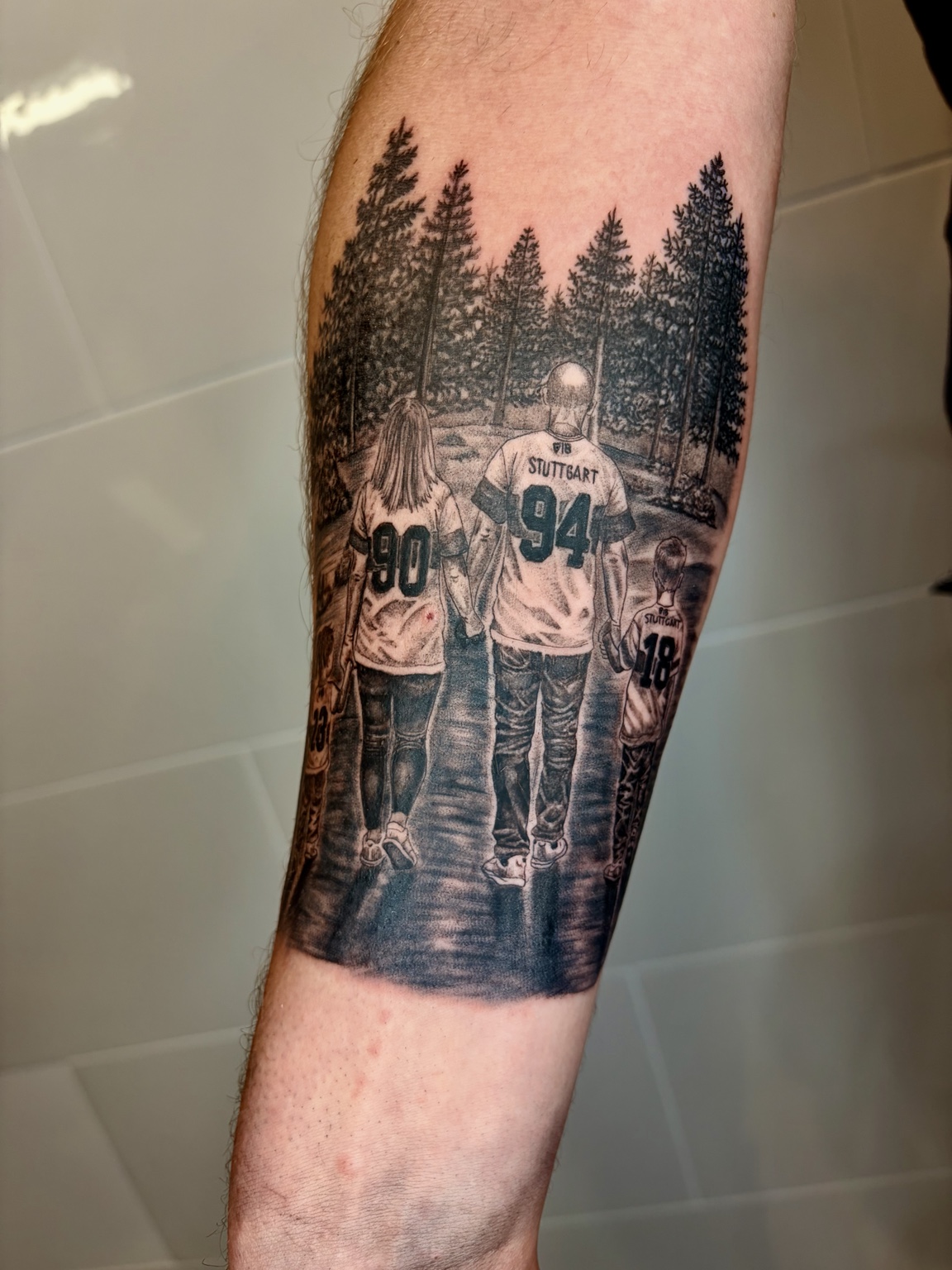 Familie mit Trikots vor einer Waldlandschaft als realistisches Unterarmtattoo